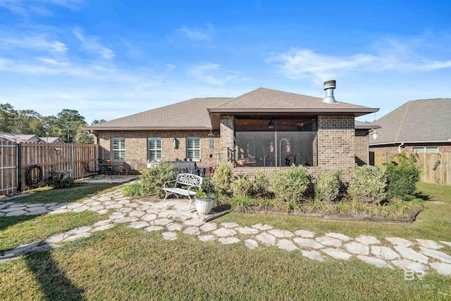 rear view of property featuring a lawn, a sunroom, and a patio