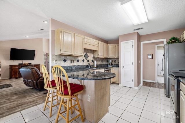 kitchen with a breakfast bar area, visible vents, open floor plan, vaulted ceiling, and stainless steel electric range oven