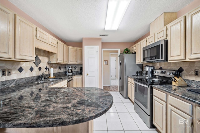 kitchen with light tile patterned floors, stainless steel appliances, a sink, dark stone counters, and light brown cabinetry