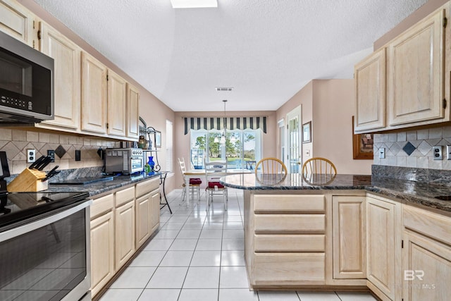 kitchen featuring light tile patterned floors, stainless steel appliances, hanging light fixtures, light brown cabinetry, and dark stone counters