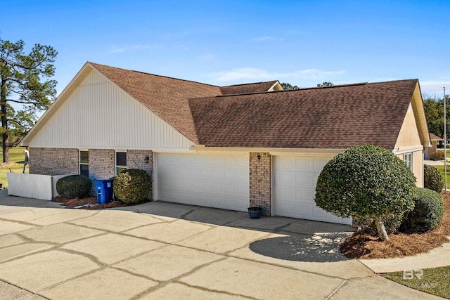 view of home's exterior with an attached garage, driveway, a shingled roof, and brick siding