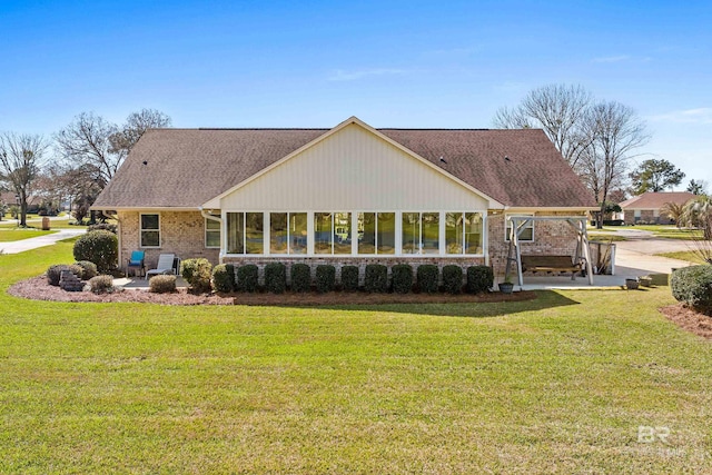 back of property with a yard, brick siding, roof with shingles, and a patio area