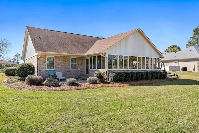 back of property featuring a shingled roof, a sunroom, brick siding, and a yard