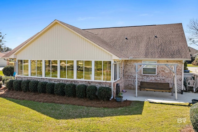 rear view of house featuring a sunroom, a patio area, a lawn, and brick siding