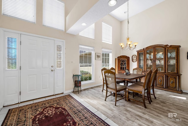 dining room with baseboards, light wood finished floors, a high ceiling, and an inviting chandelier