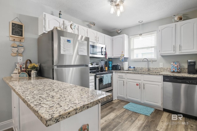 kitchen with a peninsula, stainless steel appliances, light wood-style floors, a textured ceiling, and a sink