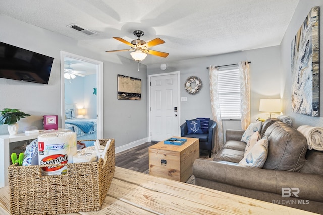 living area with visible vents, a ceiling fan, a textured ceiling, wood finished floors, and baseboards