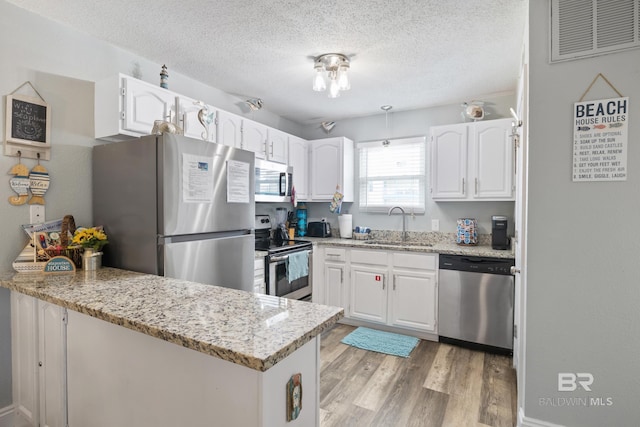 kitchen featuring visible vents, a peninsula, light wood-style flooring, a sink, and stainless steel appliances