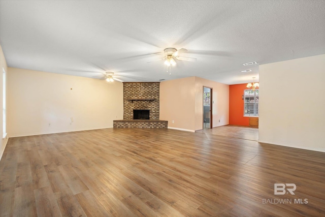 2405 Pavan Dr, Mobile, AL 36693 - unfurnished living room featuring a brick fireplace, visible vents, baseboards, wood finished floors, and ceiling fan with notable chandelier