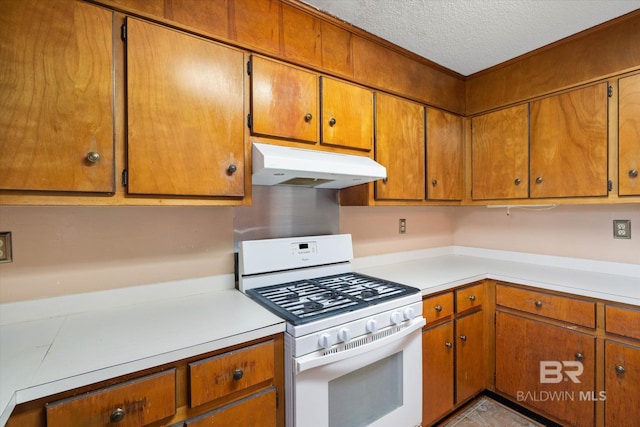 2405 Pavan Dr, Mobile, AL 36693 - kitchen with a textured ceiling, white gas range, light countertops, under cabinet range hood, and brown cabinetry