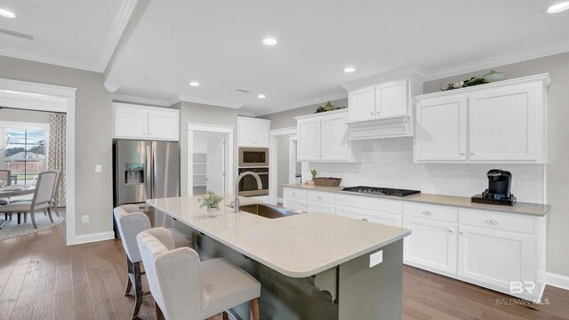 kitchen featuring appliances with stainless steel finishes, sink, white cabinets, a kitchen bar, and a kitchen island with sink