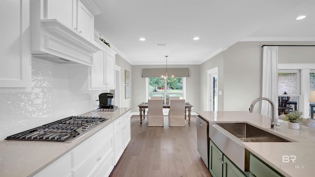 kitchen with appliances with stainless steel finishes, sink, hanging light fixtures, ornamental molding, and light hardwood / wood-style floors