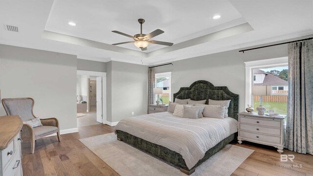 bedroom with ensuite bathroom, ceiling fan, light hardwood / wood-style floors, and a tray ceiling