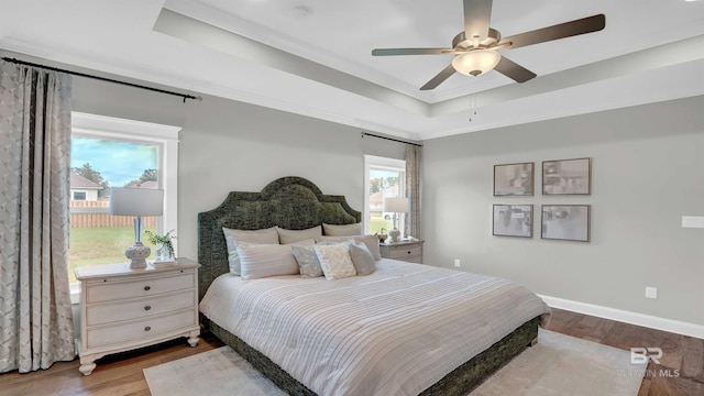 bedroom with multiple windows, wood-type flooring, ceiling fan, and a tray ceiling