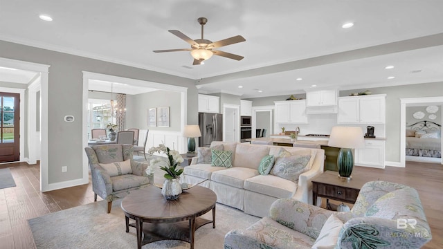 living room with ornamental molding, ceiling fan with notable chandelier, and light wood-type flooring