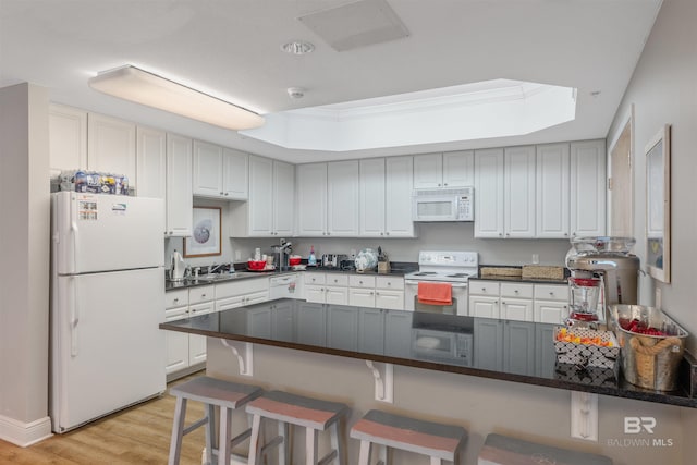 kitchen featuring white cabinetry, a tray ceiling, a kitchen bar, light hardwood / wood-style floors, and white appliances