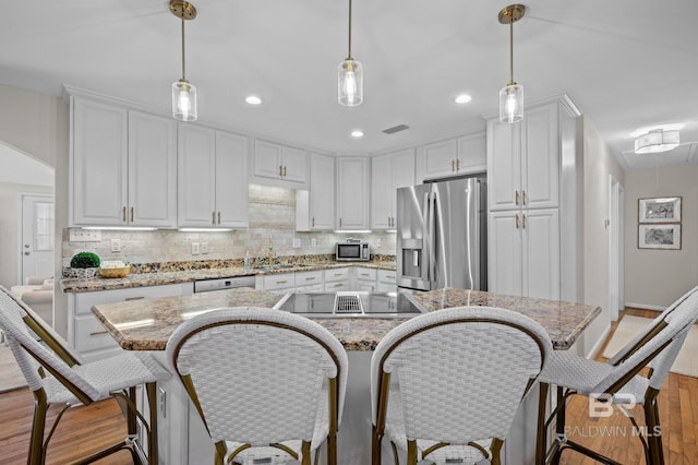 kitchen with a center island, hanging light fixtures, light stone countertops, appliances with stainless steel finishes, and white cabinetry