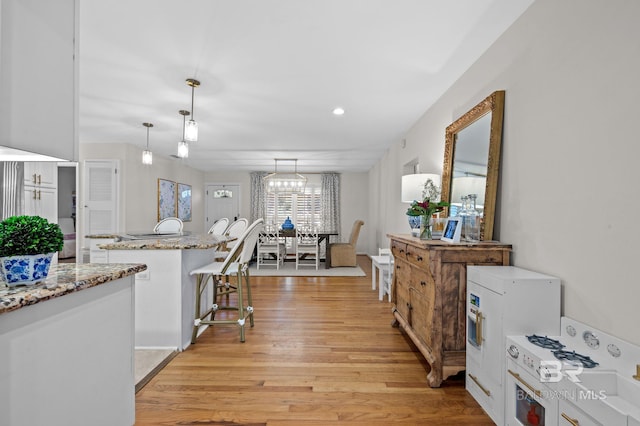 kitchen with light stone countertops, hanging light fixtures, a kitchen bar, white cabinets, and light wood-type flooring