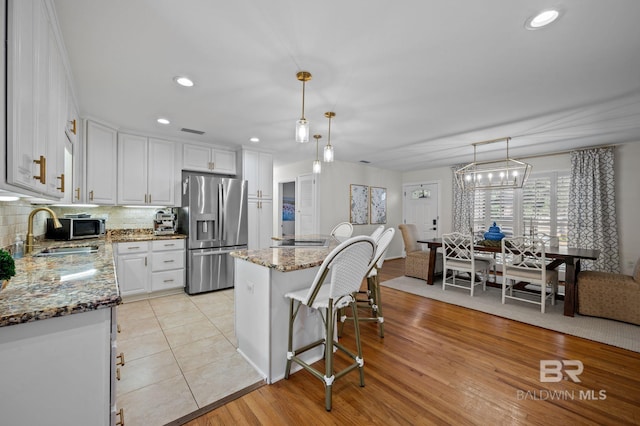 kitchen featuring stainless steel fridge with ice dispenser, sink, white cabinets, and hanging light fixtures