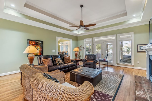 living area featuring light wood finished floors, a brick fireplace, baseboards, a tray ceiling, and french doors