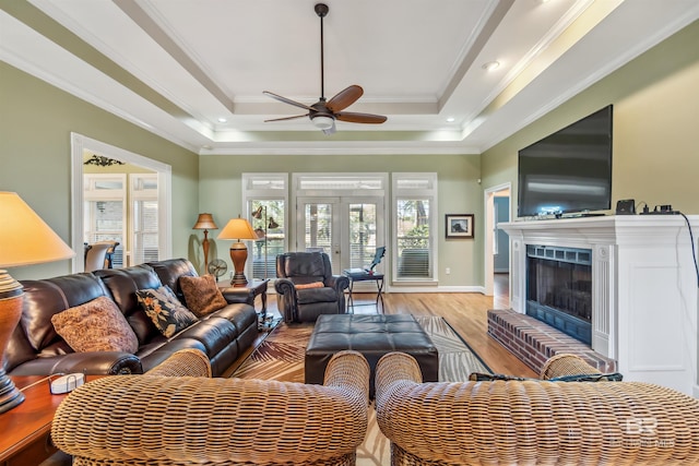 living area with a raised ceiling, a fireplace, light wood-style flooring, and crown molding