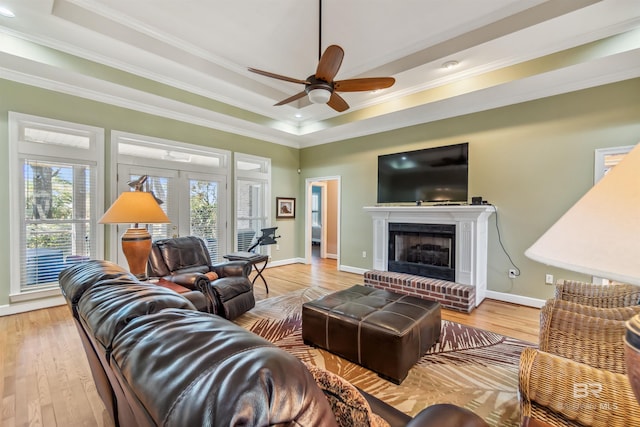 living area featuring light wood-style flooring, a brick fireplace, and a tray ceiling