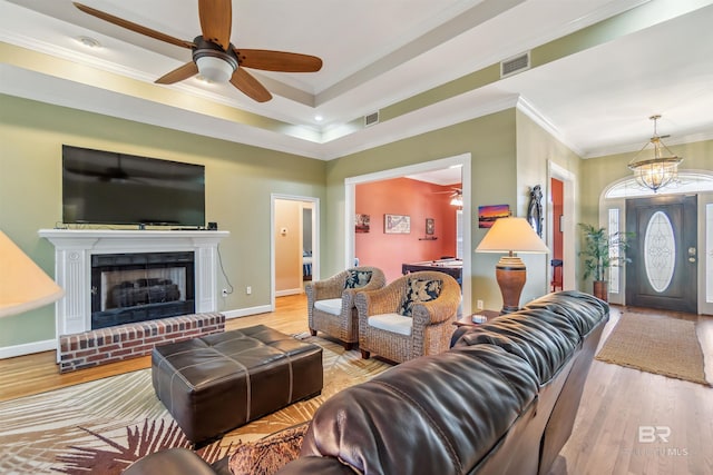 living area featuring a brick fireplace, wood finished floors, visible vents, and ornamental molding