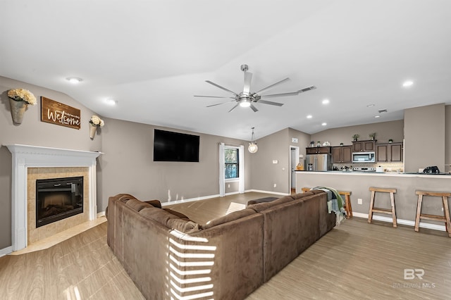 living room with light hardwood / wood-style floors, ceiling fan, lofted ceiling, and a tiled fireplace