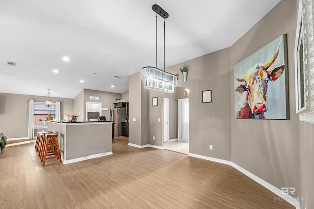 kitchen with lofted ceiling, hanging light fixtures, stainless steel fridge, light wood-type flooring, and a breakfast bar area