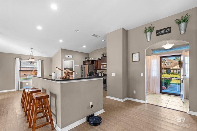 kitchen featuring a kitchen breakfast bar, light wood-type flooring, stainless steel appliances, and vaulted ceiling