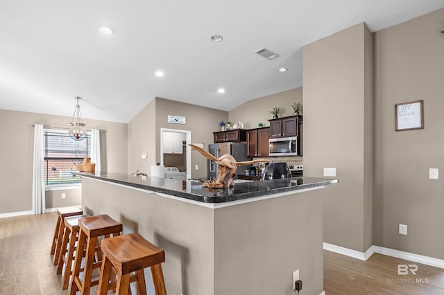 kitchen with dark brown cabinetry, stainless steel appliances, a notable chandelier, vaulted ceiling, and a breakfast bar area