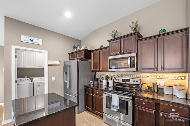 kitchen featuring washing machine and clothes dryer, stainless steel appliances, dark stone counters, lofted ceiling, and light wood-type flooring