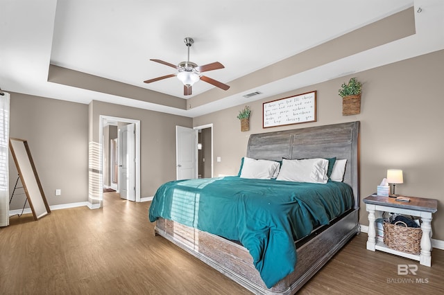 bedroom with a raised ceiling, ceiling fan, and wood-type flooring