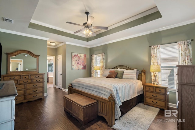 bedroom featuring visible vents, ornamental molding, wood finished floors, baseboards, and a tray ceiling