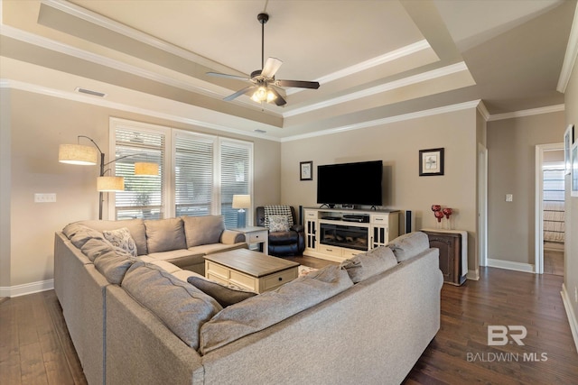 living area featuring crown molding, baseboards, ceiling fan, a tray ceiling, and a wealth of natural light