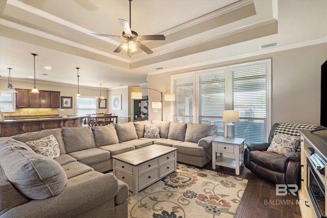 living room with ceiling fan, light wood-style flooring, a tray ceiling, visible vents, and ornamental molding