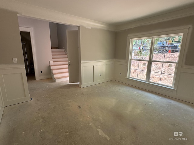 empty room with a wainscoted wall, unfinished concrete floors, stairs, and a decorative wall