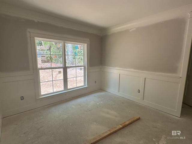 empty room featuring a wainscoted wall, concrete floors, and a decorative wall