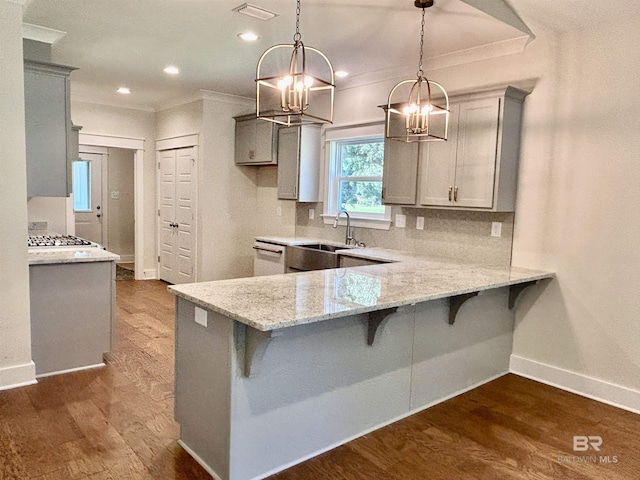 kitchen featuring a kitchen bar, a sink, hanging light fixtures, and gray cabinetry