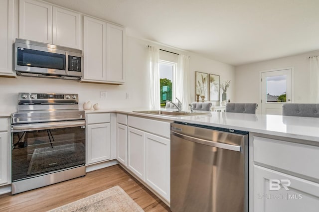 kitchen featuring light wood-style floors, light countertops, white cabinets, a sink, and appliances with stainless steel finishes