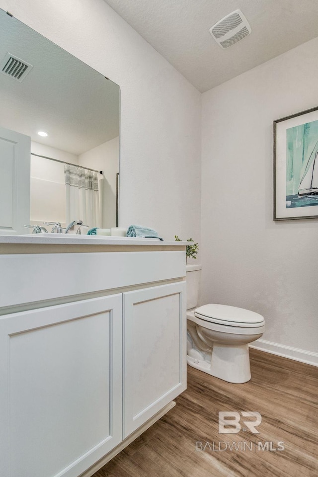bathroom featuring toilet, baseboards, visible vents, and wood finished floors