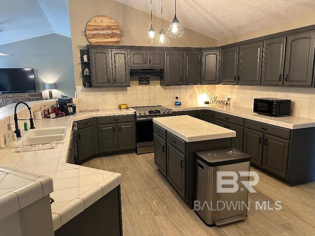 kitchen featuring tile counters, stainless steel range with electric stovetop, lofted ceiling, and sink