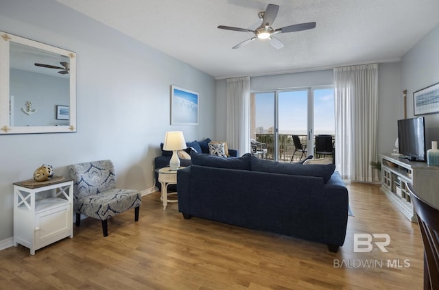 living room with ceiling fan, a textured ceiling, and light wood-type flooring