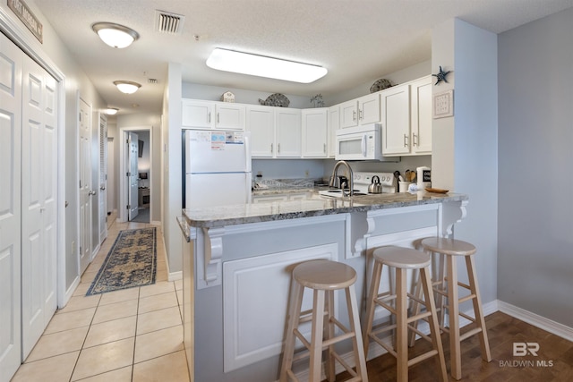 kitchen with white cabinetry, a kitchen breakfast bar, kitchen peninsula, white appliances, and light stone countertops