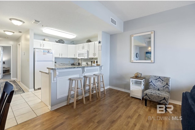 kitchen with light tile patterned floors, white appliances, a breakfast bar area, white cabinetry, and kitchen peninsula