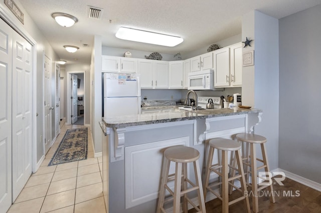 kitchen featuring white cabinetry, a breakfast bar area, kitchen peninsula, light stone countertops, and white appliances