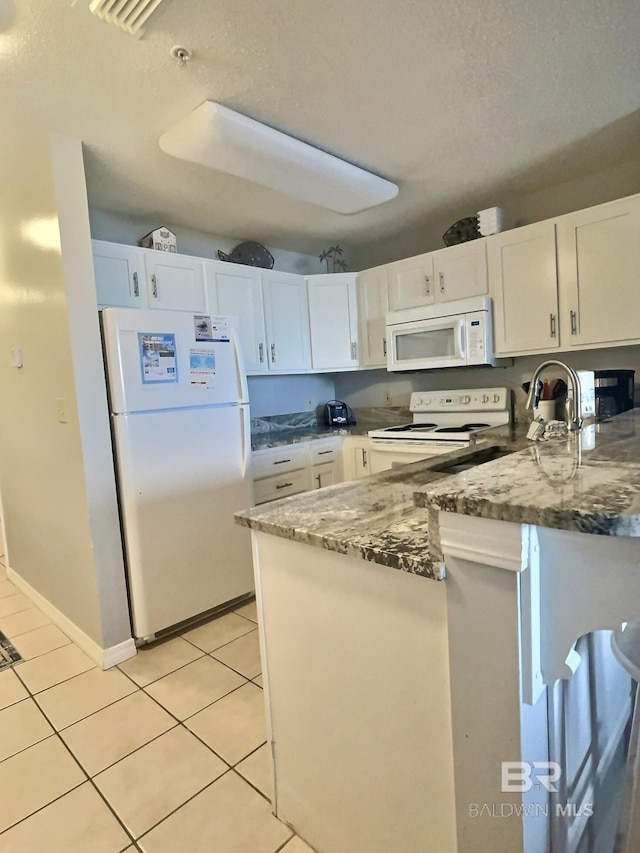 kitchen featuring light tile patterned floors, white appliances, dark stone counters, and white cabinets