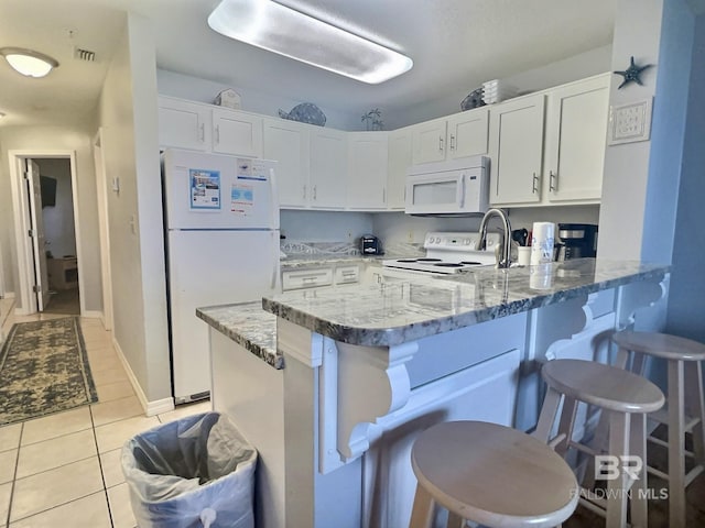 kitchen with white cabinetry, light stone countertops, a breakfast bar, and white appliances