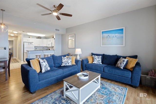 living room with ceiling fan, sink, and light wood-type flooring