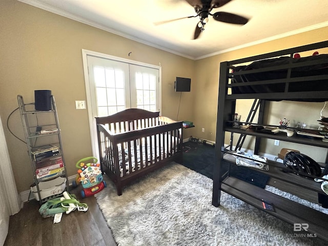 bedroom with wood finished floors, a nursery area, ceiling fan, baseboards, and crown molding